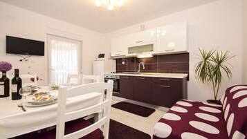 A compact kitchen with white and dark cabinets, a dining table with chairs, and a TV mounted on the wall.