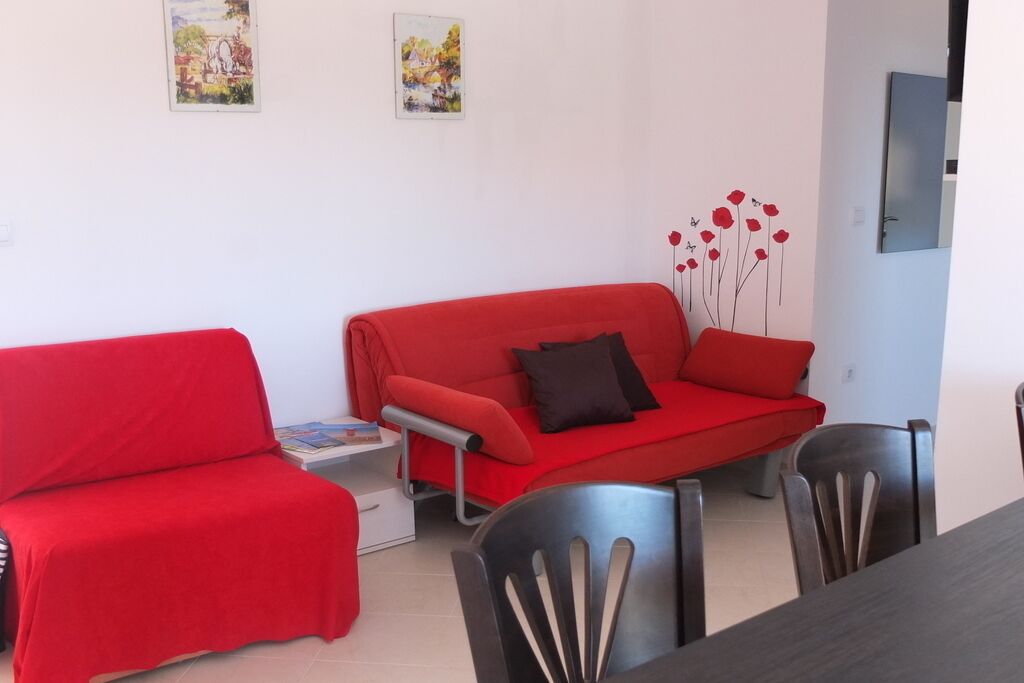 A room with two red sofas, a dining table with chairs, and two framed pictures on the wall.
