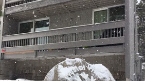 Una piedra cubierta de nieve con la inscripción "Cottage Village East", frente a un edificio con balcón de madera.