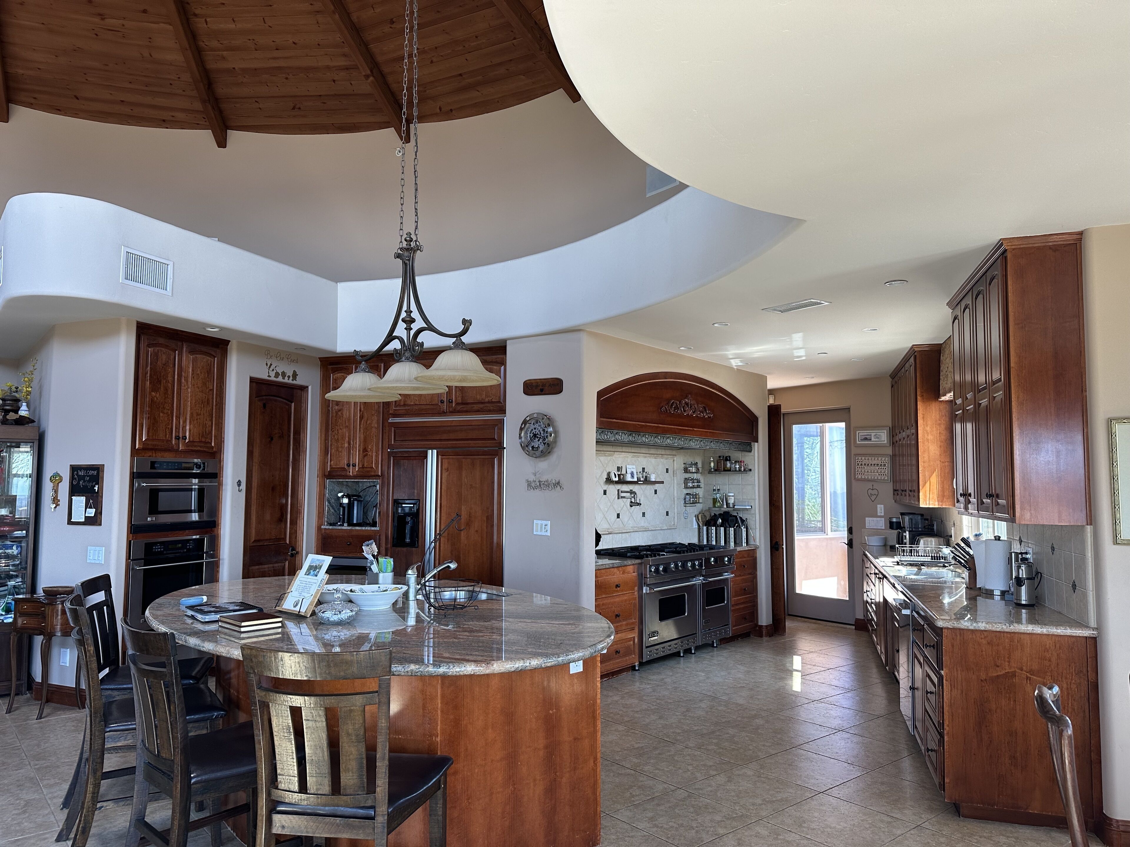 A spacious kitchen with a central island, wooden cabinets, and a large chandelier.