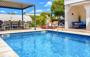 A swimming pool with lounge chairs and a covered seating area.