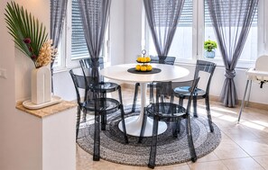 A round dining table with six chairs, a vase with dried flowers, and a fruit centerpiece.