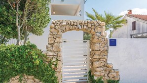 A stone archway leading to a white gate, surrounded by greenery and a white building with a blue sign. - Gorgeous home in Vrsi Mulo with sauna (Vrsi Mulo)