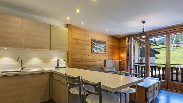 Una cocina moderna con armarios de madera, una isla central con taburetes y vistas a un paisaje verde a través de ventanas amplias.