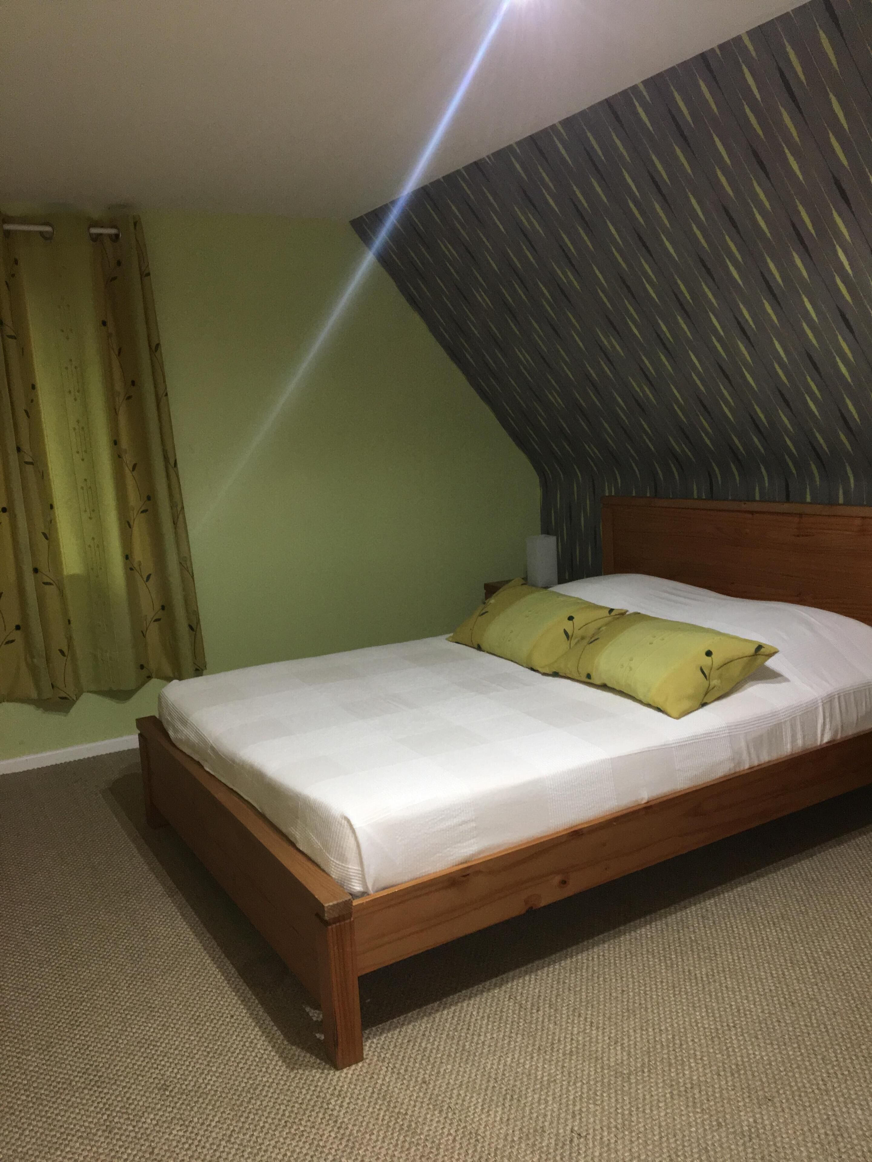 Ein Einzelbett mit hölzernem Gestell und weißer Bettwäsche, eine grüne Wand und eine gemusterte Decke.