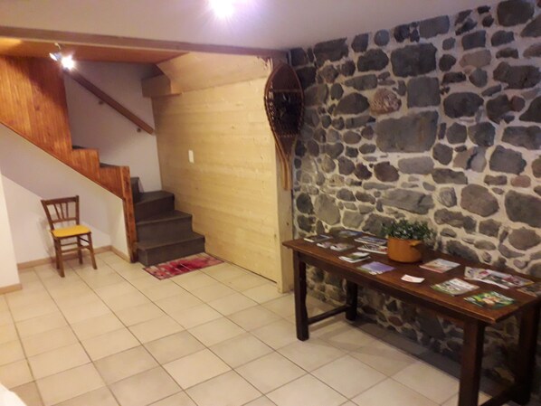 A room with a stone wall, a wooden table with magazines, a chair, and a staircase.