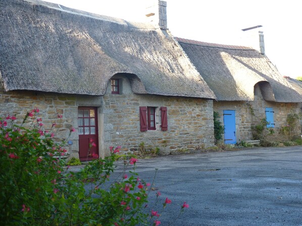 A stone building with a thatched roof, a red door, and a blue door. - house in large park near the forest, about 20 minutes from the sea. (Scaër)