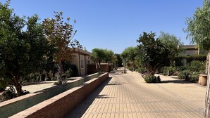 A paved walkway with brick patterns, lined with trees and shrubs, leading to a building with a tiled roof. - VILLA "LOUISA" 4P-PRIVATE POOL GROUND FLOOR PARKING COMPLEX DYARSHEMSI  (Oulad Teima)