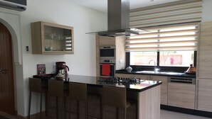 A modern kitchen with a central island, bar stools, a coffee machine, and a view through the window. - VILLA "LOUISA" 4P-PRIVATE POOL GROUND FLOOR PARKING COMPLEX DYARSHEMSI  (Oulad Teima)