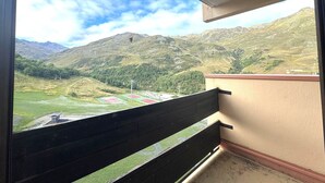 A balcony with a view of a mountainous landscape, including green fields and a small building.