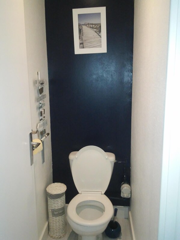 A small, narrow bathroom with a white toilet, a trash can, and a picture on the wall. - Plage de Trestraou, Apartment facing the sea, 40 m² for 4 people, Wi Fi (Perros-Guirec)