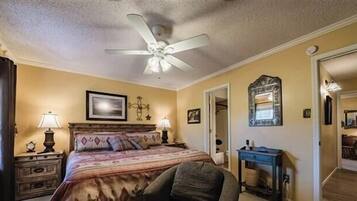 A bedroom with a bed, nightstands, a ceiling fan, a mirror, and a door leading to another room.