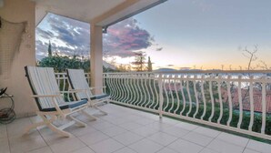Un balcón con una silla blanca y vista a una puesta de sol sobre el paisaje urbano.