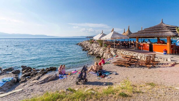Una playa con costa rocosa, zona de bar con sombrillas y vista al mar.