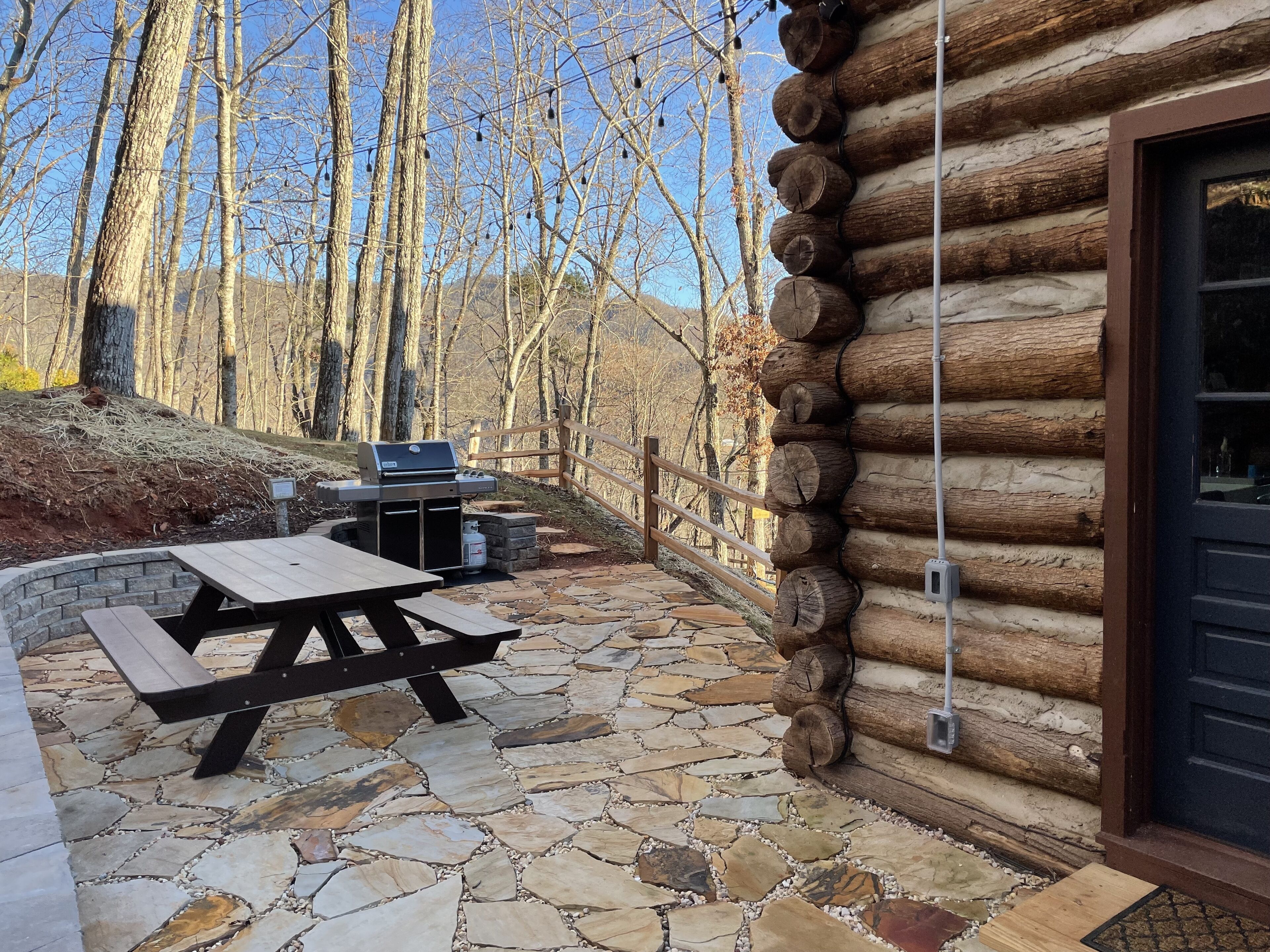 Une cabane en rondins avec un patio en pierre, une table de pique-nique et un barbecue.