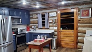 Una cocina compacta con electrodomésticos modernos, una mesa de madera y una pared rústica de troncos.