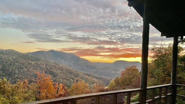 Una terraza de madera con vista a un paisaje montañoso al atardecer.