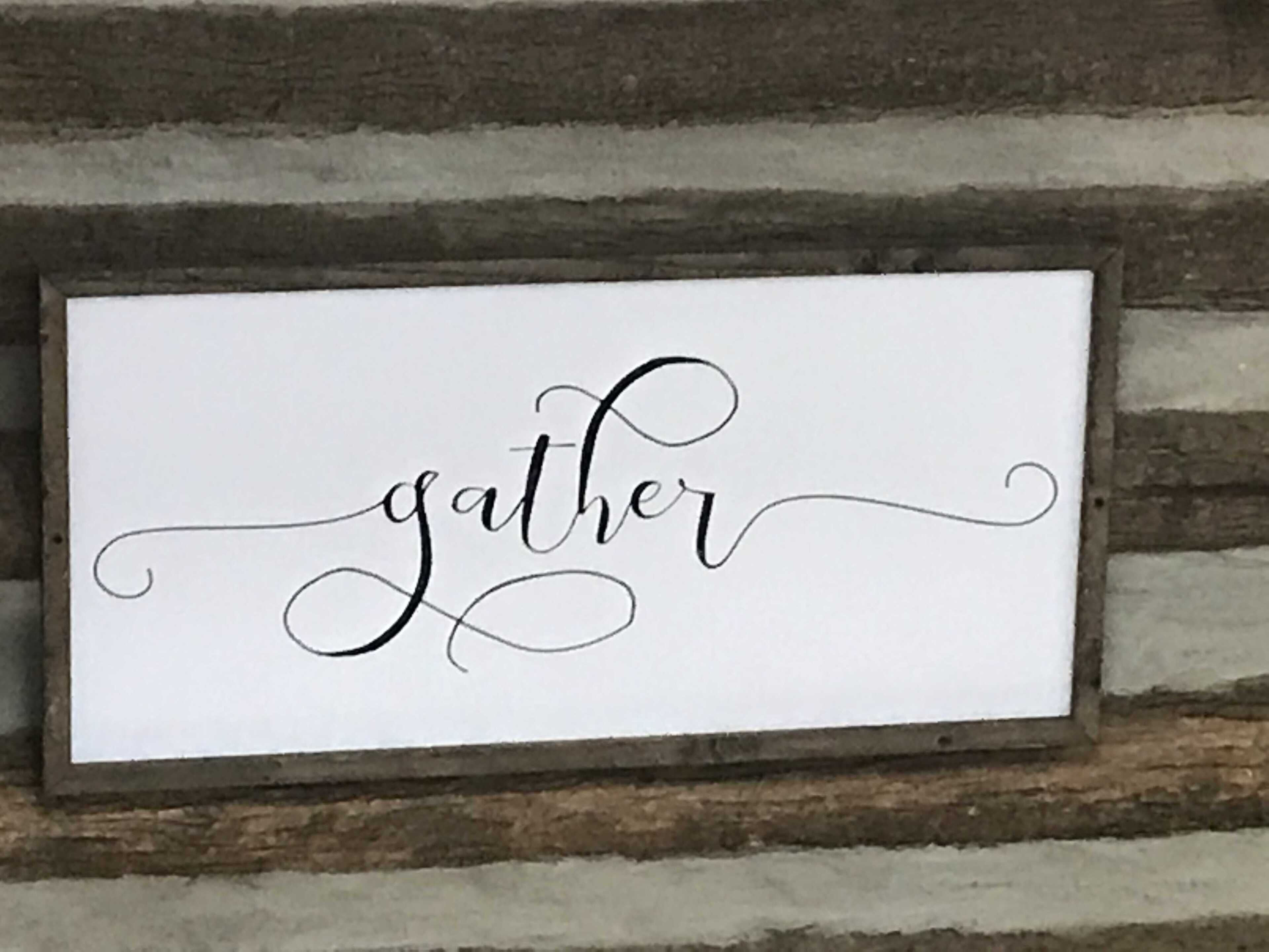 Uma placa emoldurada com a palavra 'gather' em uma escrita decorativa.