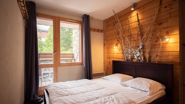 A bedroom with a large bed, wooden headboard, and a view of the outdoors through a window.