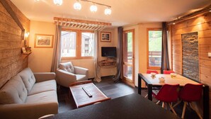 A cozy room with a sofa, a dining table with red chairs, a TV, and a window with curtains.
