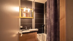A bathroom with a dark tiled wall, a wooden vanity with a sink and mirror, and a shower with a curtain.