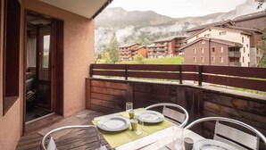 A dining area with a table set for four, overlooking a mountainous village.