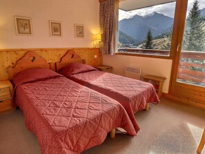 Une chambre avec deux lits, des têtes de lit en bois et une fenêtre donnant sur la montagne.