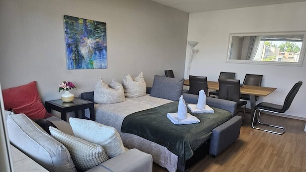 A modern hotel room with a large bed, a sofa, a desk, and a window.