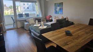 A modern living room with a wooden dining table, a sofa set, and a large window offering a view of buildings.