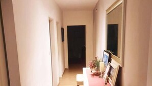 A hallway with a beige armchair, a desk with a mirror, and a door at the end.
