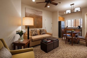 Cozy living space with a sofa, side table, and lamp, featuring a bookshelf and ceiling fan.