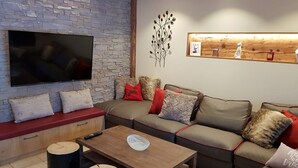 Ein modernes Wohnzimmer mit einer Steinwand, einem Flachbildfernseher, einem Holztisch und einem Sofa mit roten und beigen Kissen.