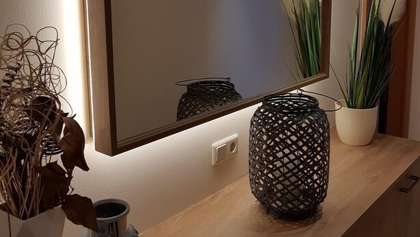 Ein modernes Badezimmer mit einem Holzbadschränkchen, einem großen Spiegel und Zierpflanzen.