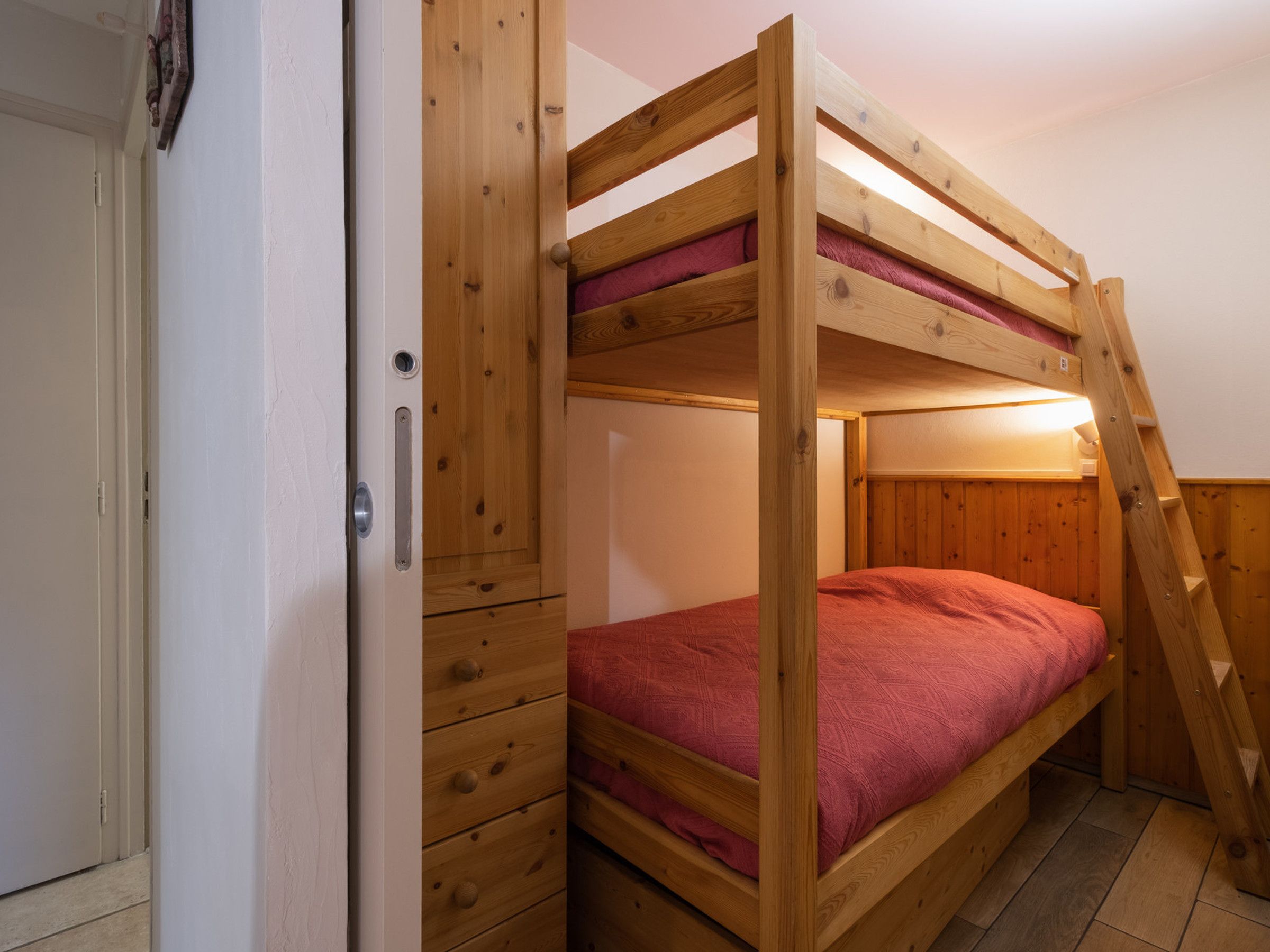 Un lit superposé avec une structure en bois, un matelas rouge et une échelle.