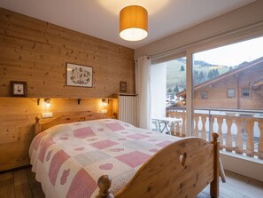 Un dormitorio de madera con una cama, un ventanal con vistas a edificios y una lámpara en el techo.