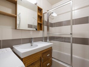 A modern bathroom with a white sink, wooden vanity, a mirror, and a glass shower enclosure.