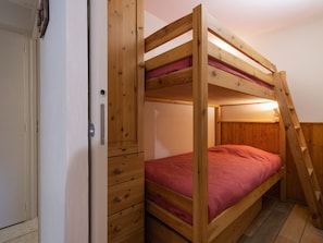Una cama litera con estructura de madera, colchón rojo y escalera.