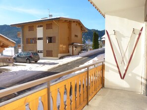 Un edificio de madera con balcón, un coche estacionado frente a él y nieve en el suelo.