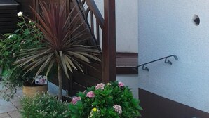 Un'area esterna coperta con una scala in legno, piante in vaso e una parete bianca.