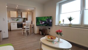 Un soggiorno moderno con televisione, un'area pranzo e una cucina sullo sfondo.