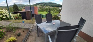A patio with a table and chairs, a small garden, and a view of a village and hills in the background.