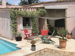A poolside area with a red chair, a green chair, and a table. There are potted plants and a stone wall. - Rare, in town and quiet, refined Mazet, private pool, flower garden (L'isle-Sur-La-Sorgue)
