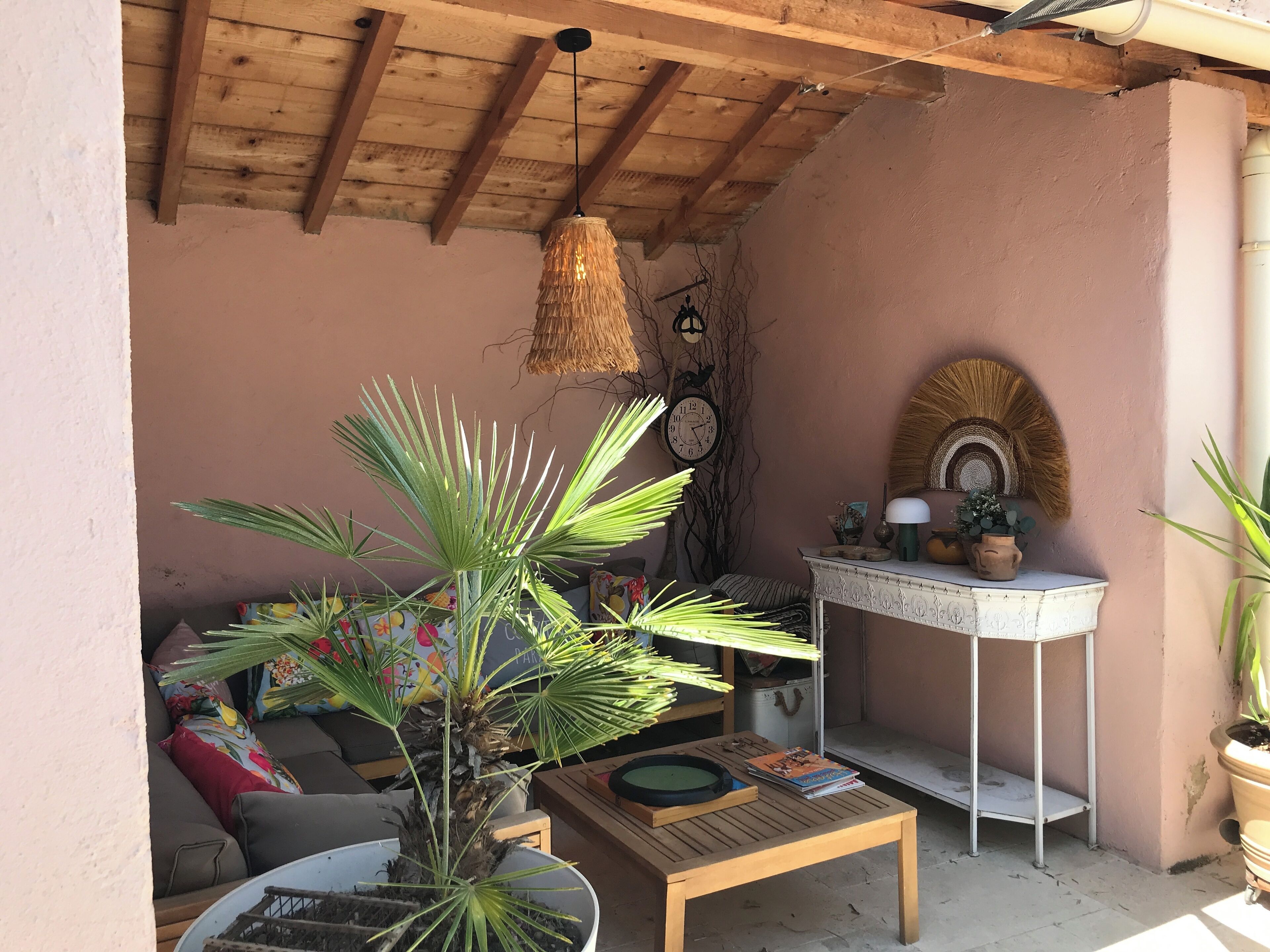 A cozy patio area with a wooden ceiling, a round table, a sofa, and a small white table with decorative items.