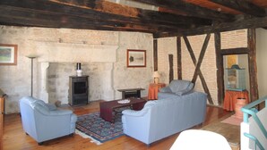 A rustic living room with exposed wooden beams, a fireplace, two sofas, and a small table. - In a listed village, half-timbered house overlooking a wooded valley (Montjoi)