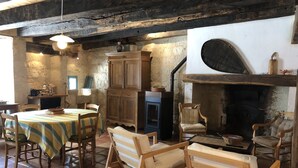 A rustic dining area with a wooden table and chairs, a fireplace, and stone walls. - In a listed village, half-timbered house overlooking a wooded valley (Montjoi)