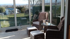 Een glazen conservatorium met rieten meubels, een glazen tafel en uitzicht op de omgeving.