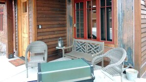 Una cabana de fusta amb un porxo, dues cadires de vimetla, una taula i una banca verda.