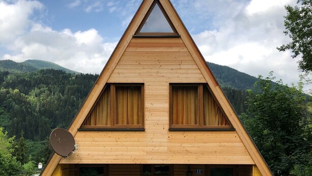Une cabane triangulaire en bois, dotée d’une grande fenêtre et d’un banc à l’avant.
