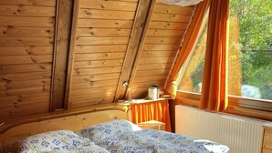 Un lit en bois dans une pièce dont le plafond est en pente, avec une fenêtre ornée de rideaux et un radiateur.