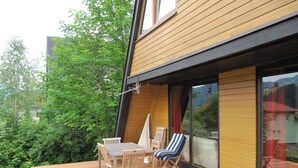 Une terrasse en bois avec une table et des chaises, une porte-fenêtre coulissante et une vue sur la verdure et les bâtiments.